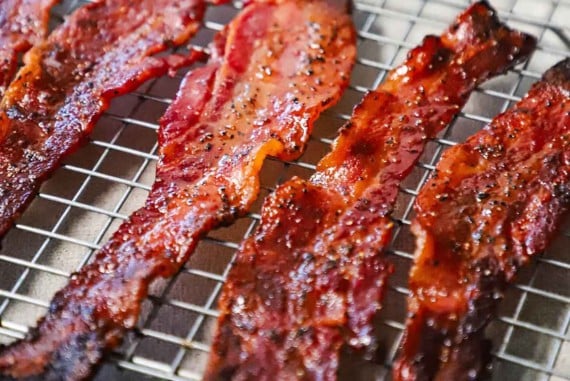 A straight-on view of cooked strips of maple pepper bacon resting on two baking racks.