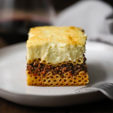 A straight-on view of a perfectly square piece of Greek pastitsio on a white dinner plate.