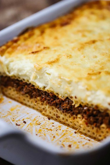 A view looking into a lasagna dish that is filled with pastitsio which consists of a bottom layer of tubular pasta, topped with a meat sauce, and then topped off with a thick Greek bechamel sauce.