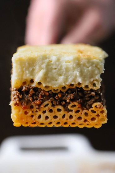 A person holding up a spatula that has a perfectly square slice of pastitsio on it.