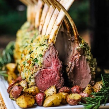 A straight-on view of two roast rack of lamb persillade that are on a platter with the bones interlocking above the chops forming a cathedral-looking roast.