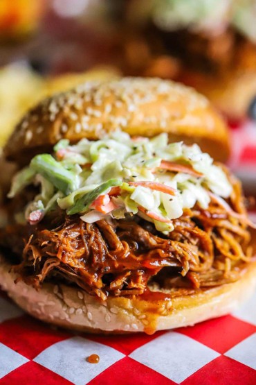 A straight-on view of a slow cooker pulled pork sandwich that is topped with coleslaw and drizzled with Carolina barbecue sauce.