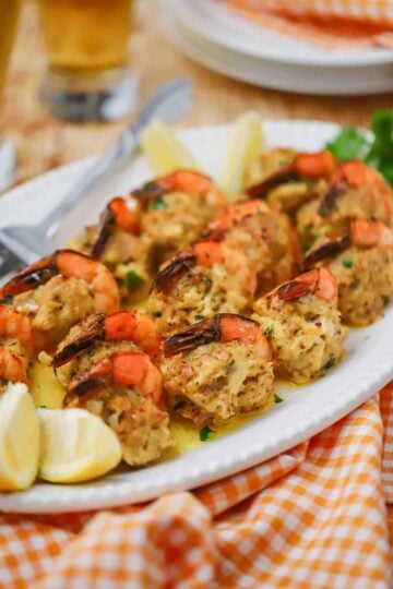 A close-up view of a white platter filled with crab-stuffed shrimp with lemon wedges nearby.