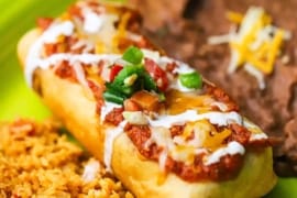 A straight-on view of an untouched beef chimichanga on a green platter flanked by a serving of Mexican rice and refried beans on the other side.
