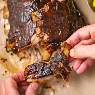 A person holding a baby back rib that has been pulled from a rack of slow cooker baby back ribs.