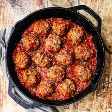 An overhead view of a large cast-iron skillet filled with Italian meatballs resting in a layer of homemade marinara sauce.