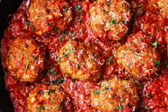 An overhead view of a large cast-iron skillet filled with Italian meatballs resting in a layer of homemade marinara sauce.