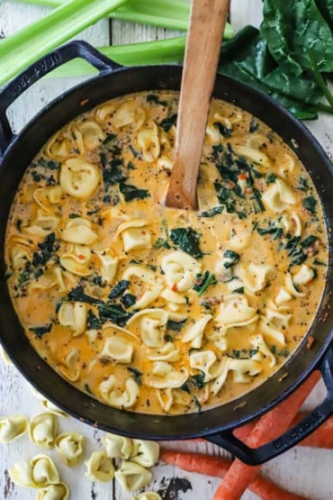 An overhead view of a black cast-iron pot filled with creamy tortellini soup with sausage and spinach.