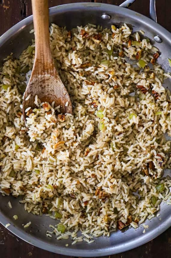 An overhead view of a large silver skillet filled with a herbed rice pilaf with toasted pecans.
