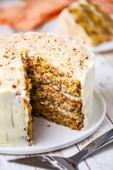 A straight-on view of a carrot cake with three layers and a tropical cream cheese icing that is topped with toasted coconut flakes.