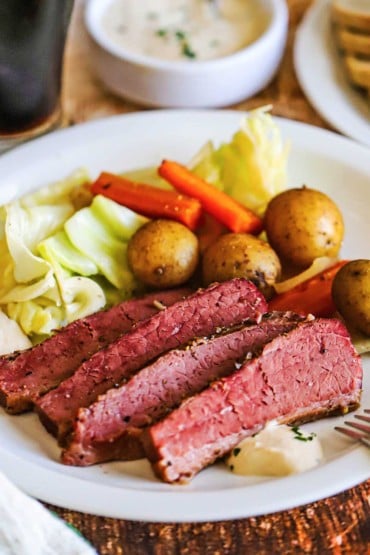 A dinner plate filled with a serving of slices of corned beef and cabbage with cooked baby potatoes and carrots.
