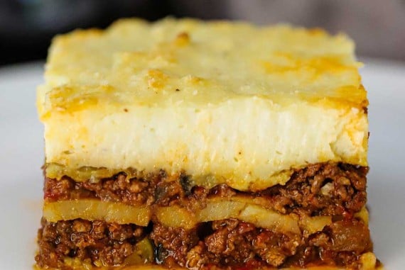 A straight-on view of a perfectly square piece of homemade moussaka sitting on a white dinner plate.