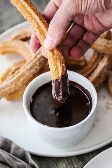 A person holding a homemade churros that has been dipped into a small bowl of chocolate sauce.