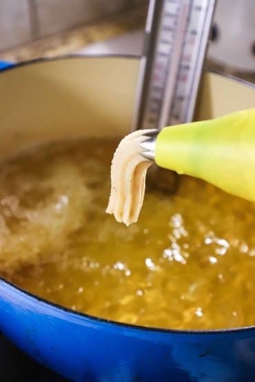 A close-up view of churros dough being squeezed out of a yellow pastry bag into a Dutch oven that is filled with hot oil.