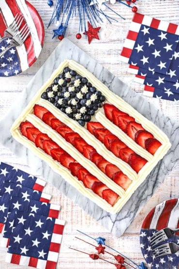 An overhead view of a cake that is decorated with blueberries, sliced strawberries, and vanilla icing to look like an American flag.