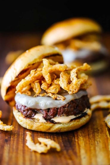 A straight-on view of a smoked steakhouse burger topped with melty provolone cheese and crispy onion strips and a layer of steak sauce aioli on the bottom bun.