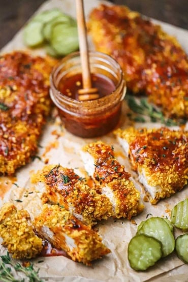 A straight-on view of a cutlet of hot honey chicken that has been cut into strips and drizzled with hot honey sauce and is surrounded by more cutlets and butter pickles.