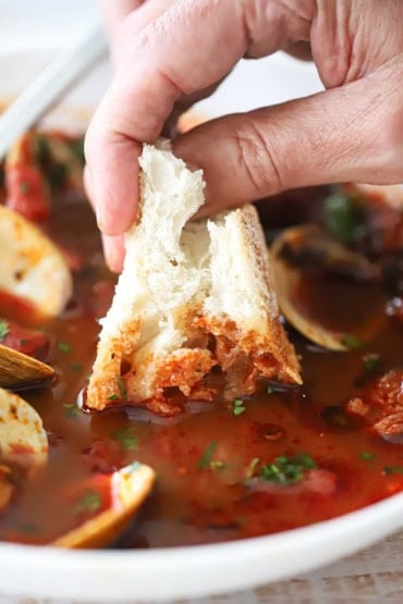 A close-up view of a person dunking a piece of bread into a bowl of Portuguese-style clam chowder.