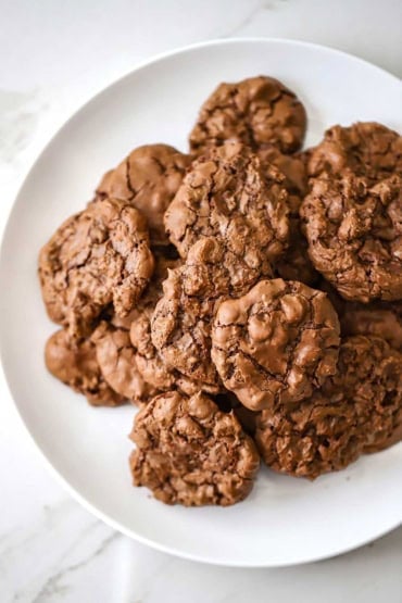 An overhead view of a pile of double chocolate chip cookies sitting on a white plate.