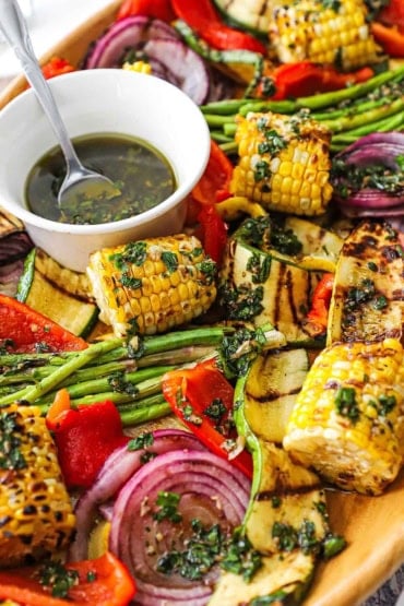 A straight-on view of grilled vegetables with Italian dressing all resting on a large bamboo oval platter.