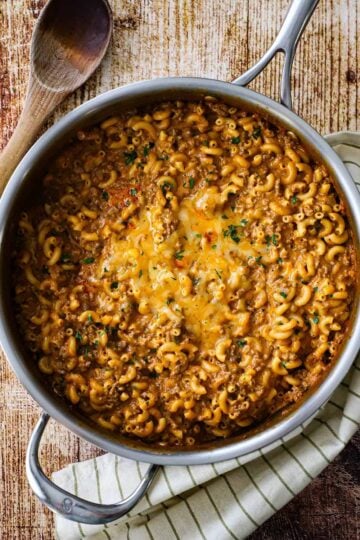 An overhead view of a large silver skillet filled with homemade cheesy hamburger helper garnished with finely chopped Italian parsley.