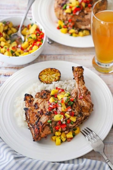 A white dinner plate filled with a serving of Jamaican jerk chicken that is topped with a mango salsa and resting on a bed of coconut rice.