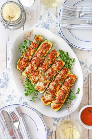 An overhead view of an antique platter filled with stuffed zucchini boats that are topped with melty cheese and surrounded by sprigs of parsley.