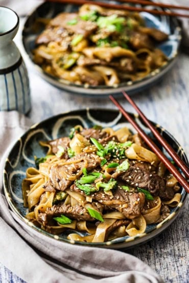 A straight-on view of two color dinner plates filled with servings of beef and broccoli chow fun.