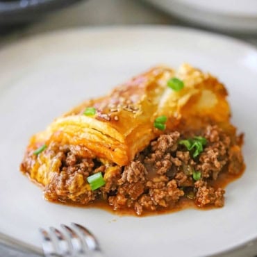 A close-up view of a single serving of sloppy Joe casserole on a white dinner plate and is garnished with chopped scallions.