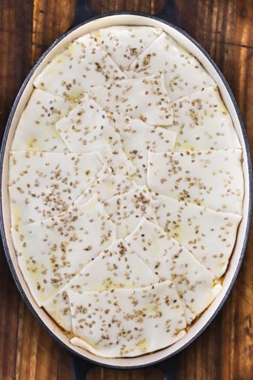 An overhead view of an oval baking dish that is filled with an uncooked sloppy Joe casserole that is topped with strips of puff pastry and topped with sesame seeds.