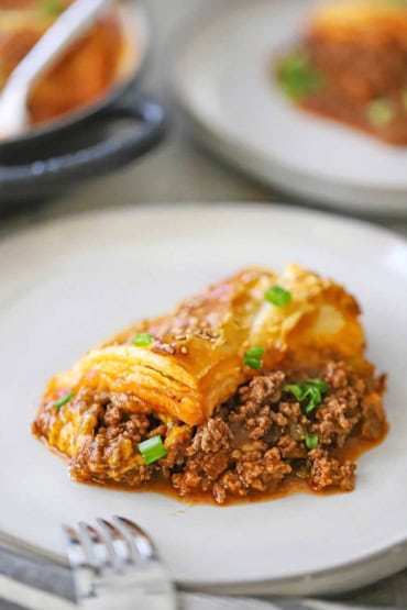 A close-up view of a single serving of sloppy Joe casserole on a white dinner plate and is garnished with chopped scallions.