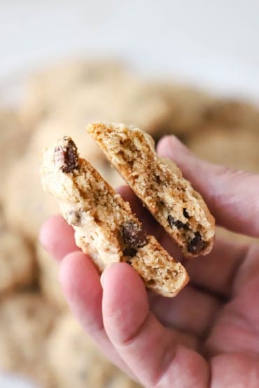 A person holding up a homemade oatmeal raisin cookie that has split in half with the interior of the cookie revealed.