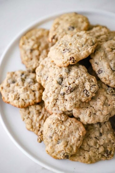 An overhead view of a circular white platter filled with a pile of homemade oatmeal raisin cookies.