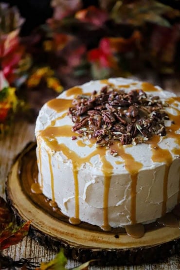 A straight-on view of a caramel layer cake that has homemade caramel drizzled over the tops and sides as well as circular pile of pecans on the top center of the cake.