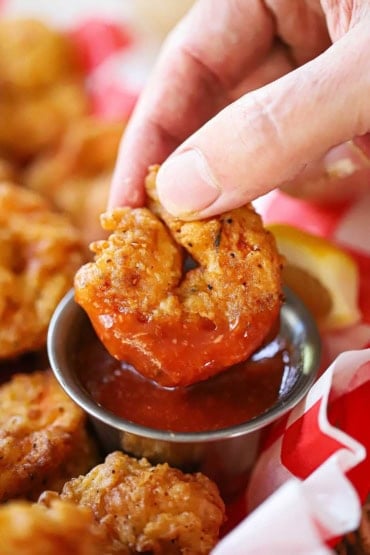 A close-up view of a person plunging a Southern fried shrimp into a small metal bowl of homemade cocktail sauce.