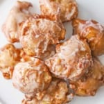 An overhead view of a pile of homemade apple fritters resting on a white circular serving platter.