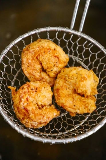 An overhead view of three Southern-fried shrimp that are being raised from hot oil in a metal spider.