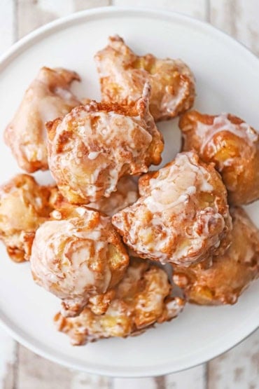 An overhead view of a pile of homemade apple fritters resting on a white circular serving platter.