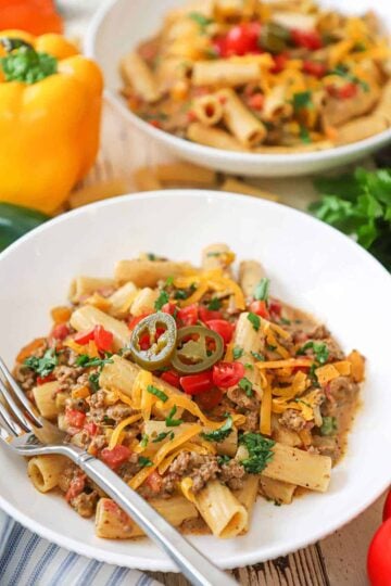 A straight-on view of two white bowls filled with Tex-Mex pasta with colorful bell peppers and cilantro sitting nearby.