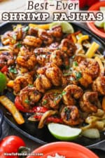 A straight-on view of a large fajita skillet filled with shrimp fajitas resting on sautéed onions and bell pepper strips with lime wedges on the side.