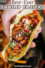 A close-up view of a person holding a prepared shrimp fajita garnished with pico de gallo, cotija cheese, and chopped fresh cilantro.