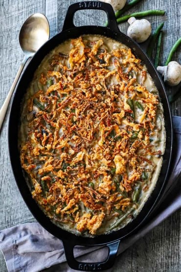 An overhead view of a large black oval baking dish that is filled with an untouched gourmet green bean casserole that is topped with fried onion strips.