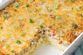 A straight-on view of a 9-inch by 13-inch white casserole dish that is filled with the best breakfast casserole with a portion of it missing and revealing the filling of the dish.