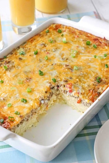 A straight-on view of a 9-inch by 13-inch white casserole dish that is filled with the best breakfast casserole with a portion of it missing and revealing the filling of the dish.