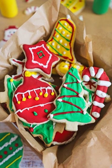 An overhead view of a box that is lined with brown wax paper and is filled with colorful homemade Christmas cookies.