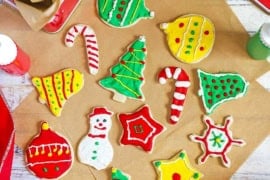 An overhead view of a collection of colorful homemade Christmas cookies that in the shape of bells, ornaments, tress, snowmen, and bells.