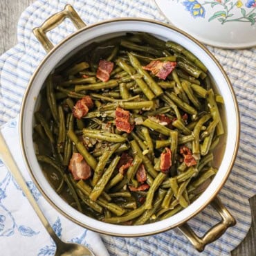 An overhead view of a pot of Southern-style green beans that have pieces of cooked bacon visible throughout and on top of the cooked beans.