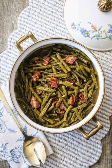 An overhead view of a pot of Southern-style green beans that have pieces of cooked bacon visible throughout and on top of the cooked beans.