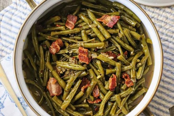 An overhead view of a pot of Southern-style green beans that have pieces of cooked bacon visible throughout and on top of the cooked beans.