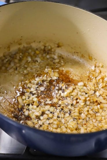 A straight-on view of chopped onions being sautéed in an oval Dutch oven over a gas stove.